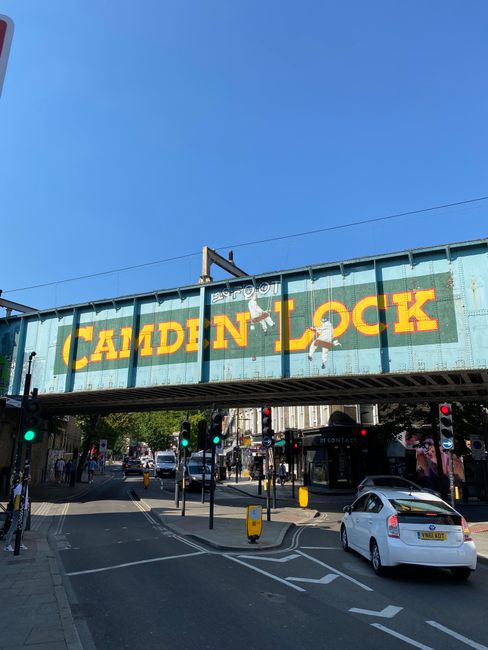A three-storey brick building with large arched windows on each floor, located on a busy street corner. The building features a prominent sign with the text 'CAMDEN LOCK' in white letters, arching acr